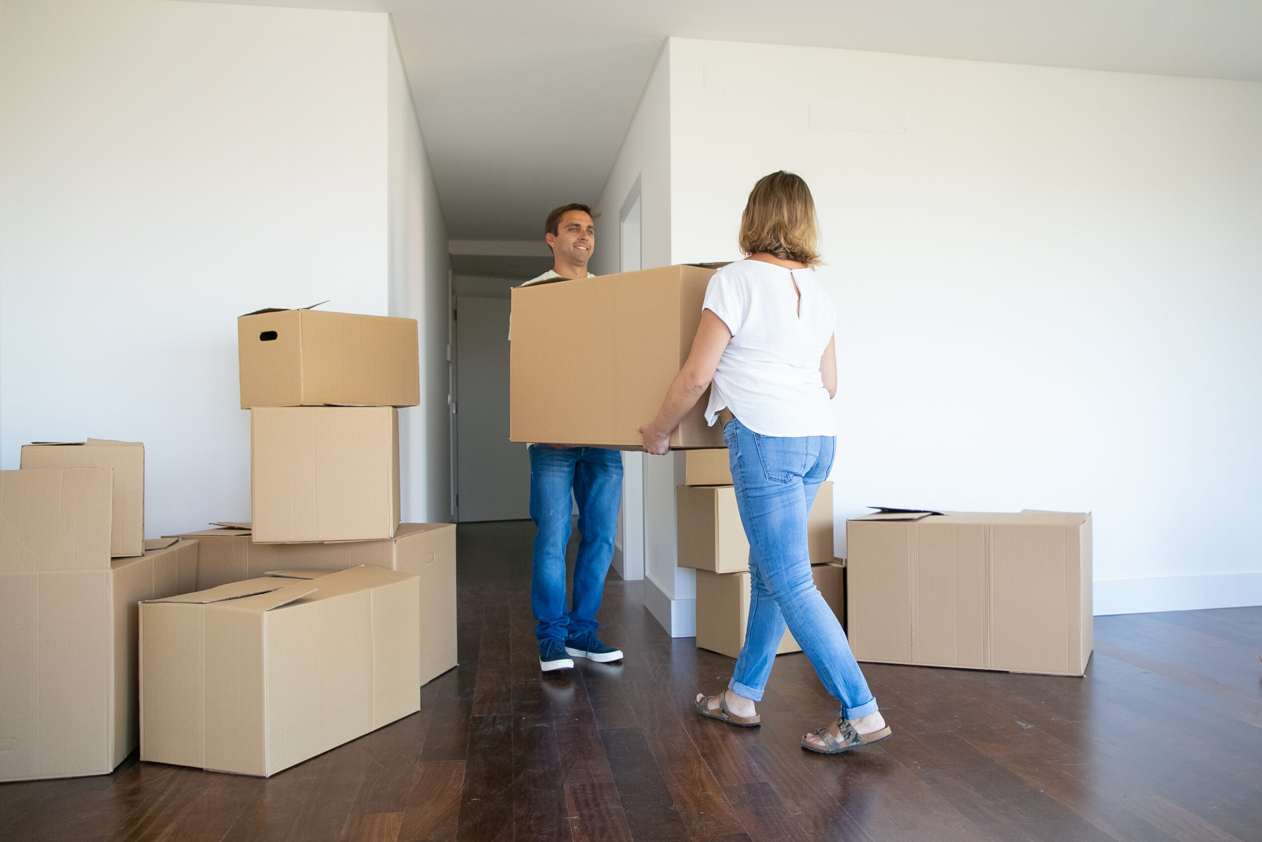 Married couple leaving apartment, carrying cartoon box to entrance together. Back view. Relocation concept