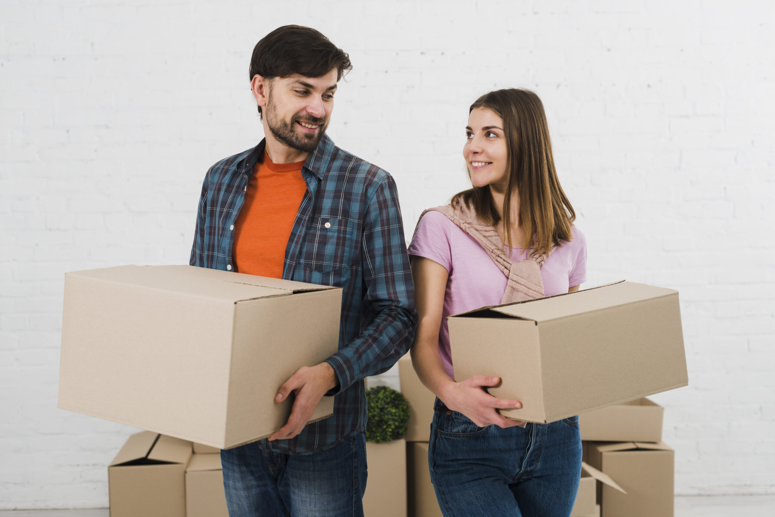 smiling-young-couple-holding-cardboard-boxes-hand-looking-each-other